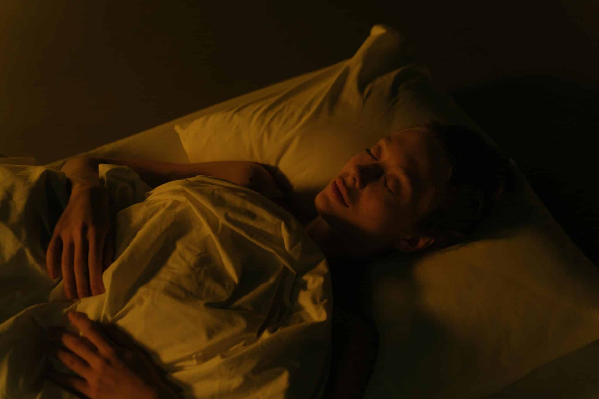 Woman lying in bed under a blanket with soft morning light, symbolizing restful deep sleep routine and calm.